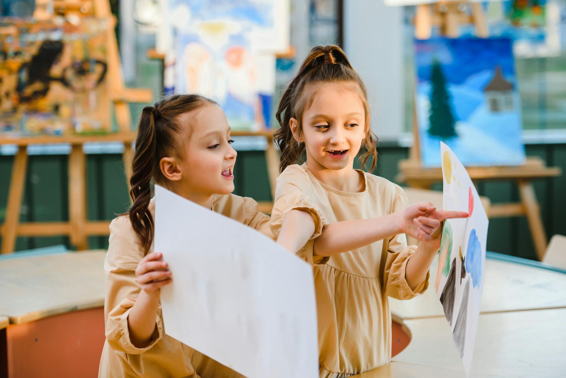 Dwie dziewczynki pokazują sobie swoje prace plastyczne w klasie