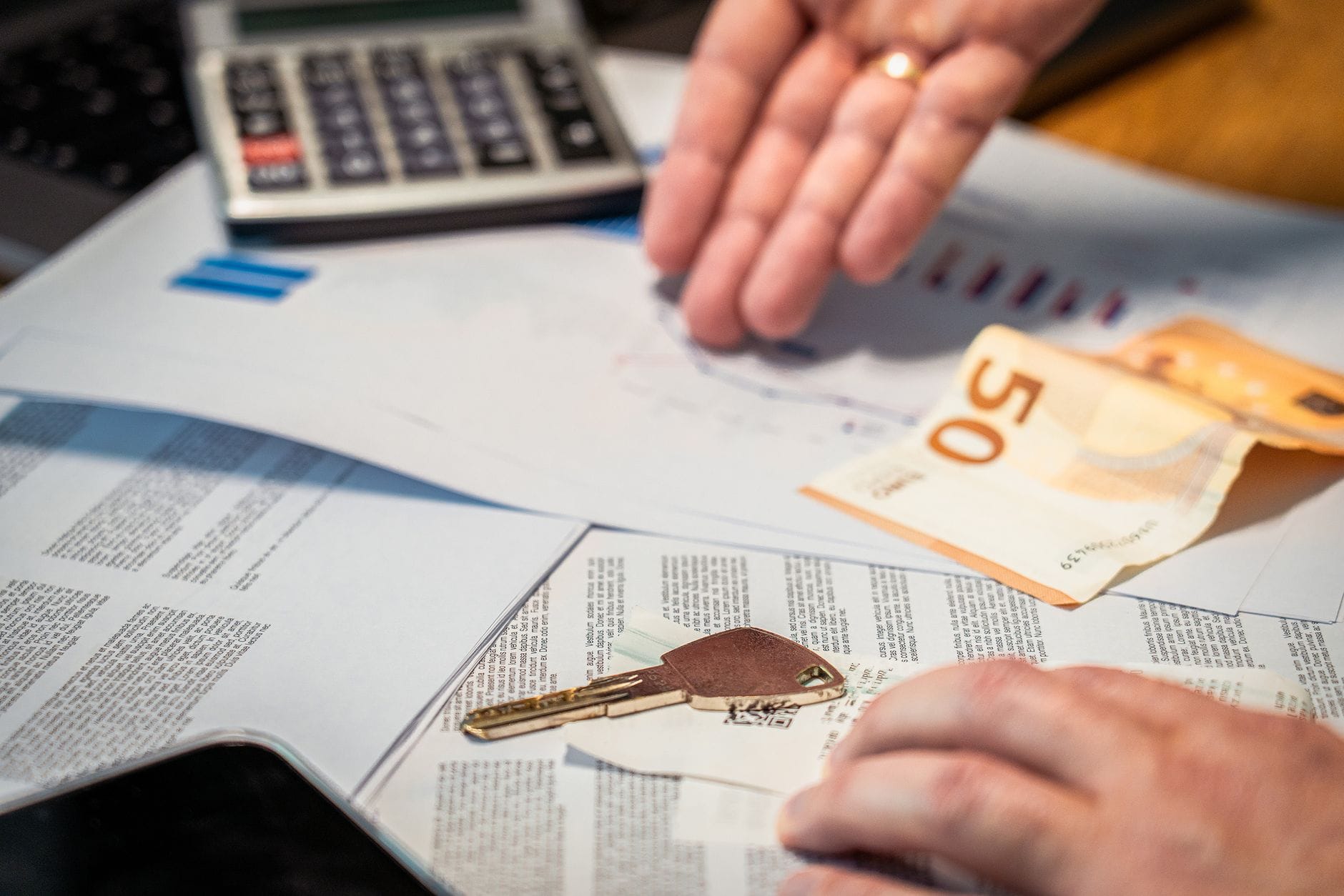 Dłonie nad dokumentami finansowymi, banknotem 50 euro i kluczykiem