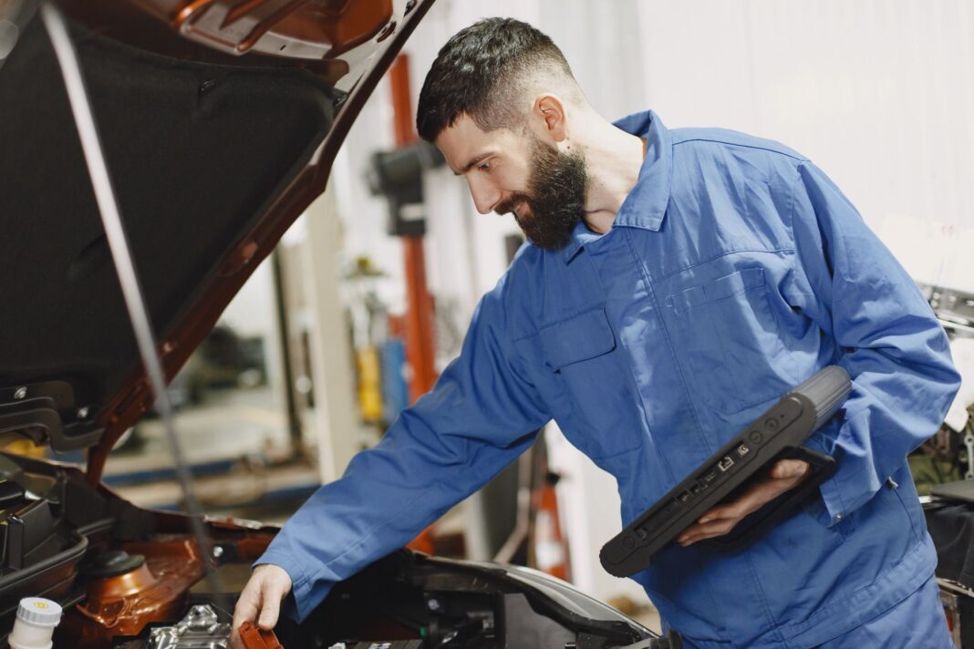 Mechanik w niebieskim kombinezonie sprawdza silnik samochodu w garażu